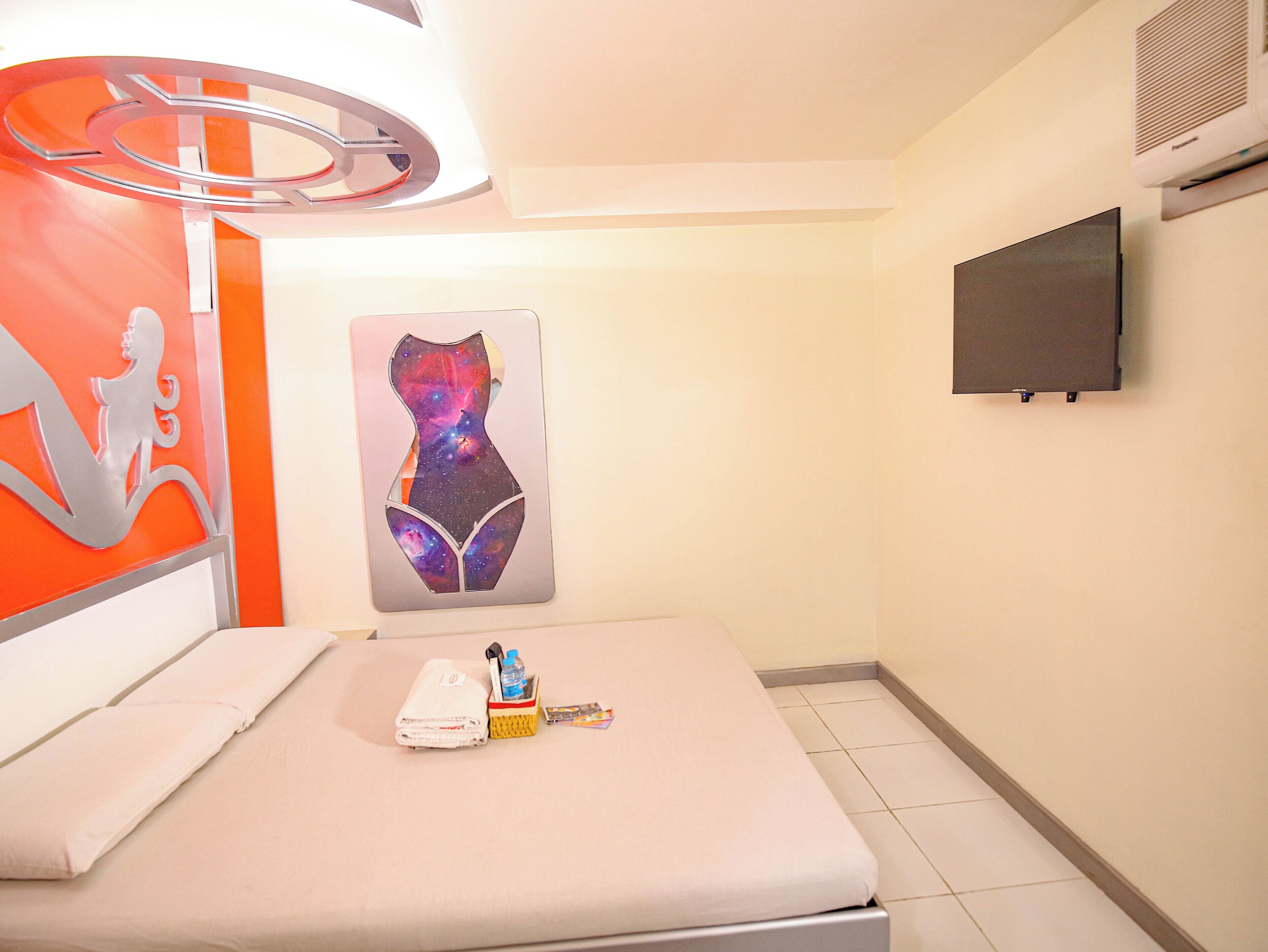 A hotel room with a bed, a wall-mounted TV, and a painting of a galaxy.