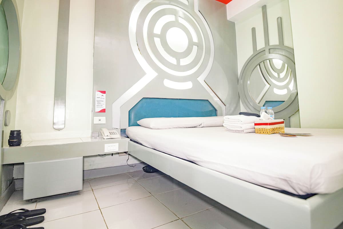 A modern hotel room with a bed, a bedside table, a mirror, and a wall with abstract design.