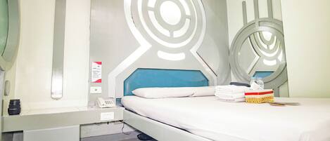 Habitación de hotel moderna con cama, mesita de noche, espejo y pared con diseño abstracto.