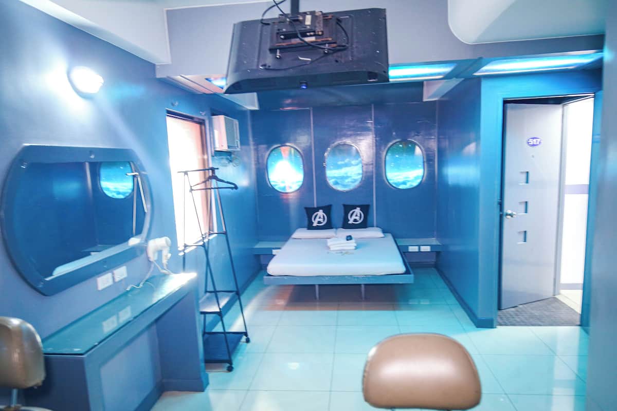 A room with a bed, a desk, a chair, and a large window with a view.