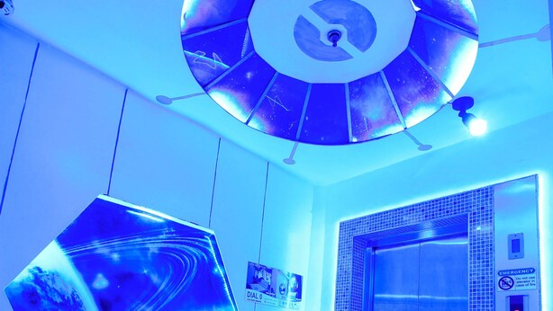 A modern elevator with a metallic finish, a blue-lit ceiling, and a hexagonal light fixture. - Astrotel Monumento (Caloocan)