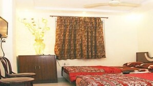 Un dormitorio con dos camas, cabeceros de madera, una mesita de noche, una silla, una lámpara, una cortina y un cuadro en la pared.