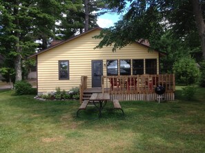 A yellow cabin with a wooden deck, picnic table, and barbecue grill.