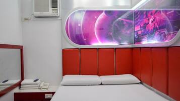 A hotel room with a modern design, featuring a bed with white linens, a red padded headboard, and a large window with a view of a space-themed digital display.