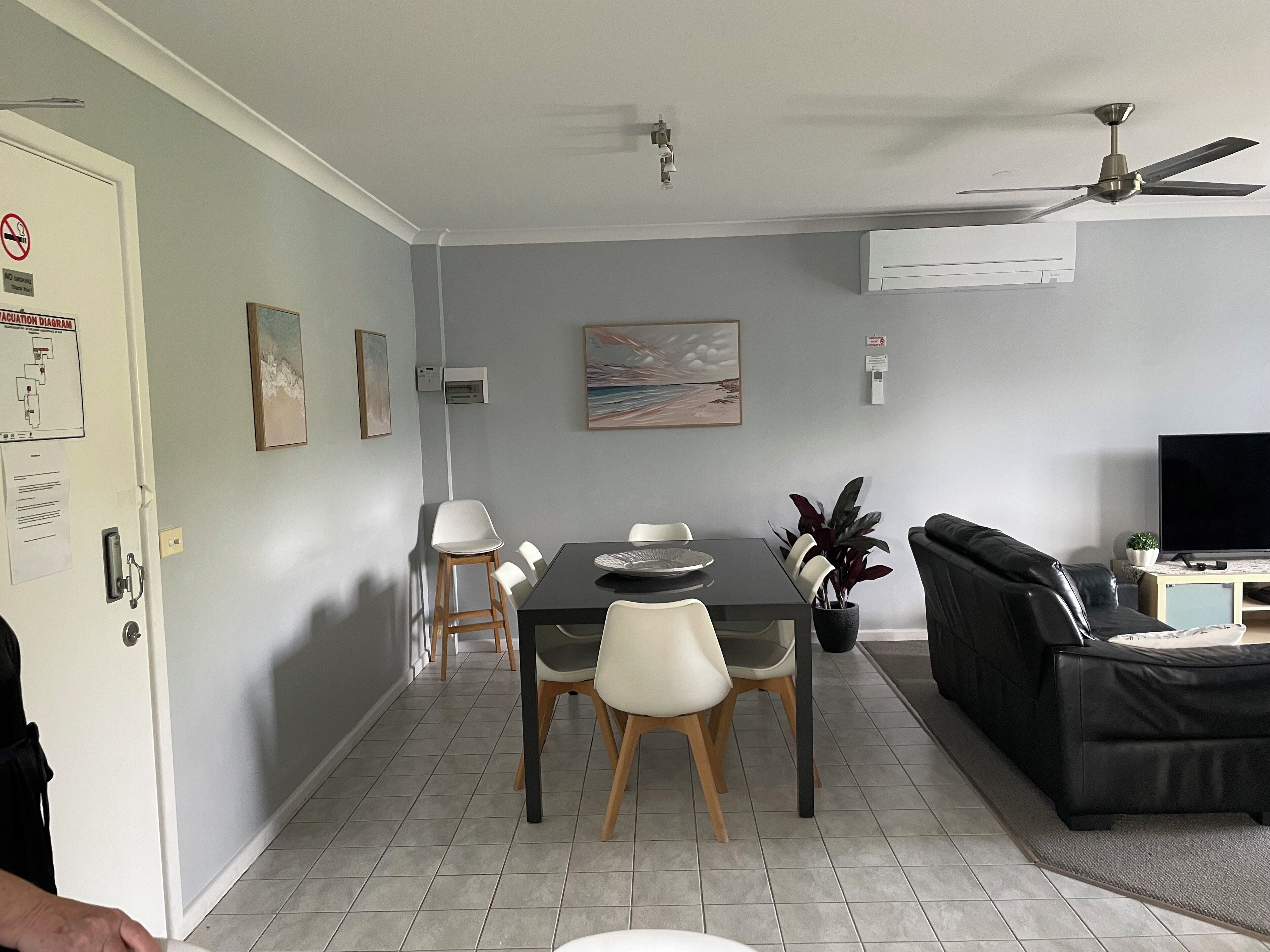A dining area with a table and chairs, a black sofa, a television, and a ceiling fan.