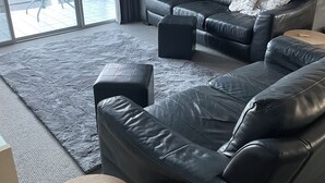 Un salon moderne avec un canapé en cuir noir, une petite table d’appoint ronde en bois et un grand tapis gris.