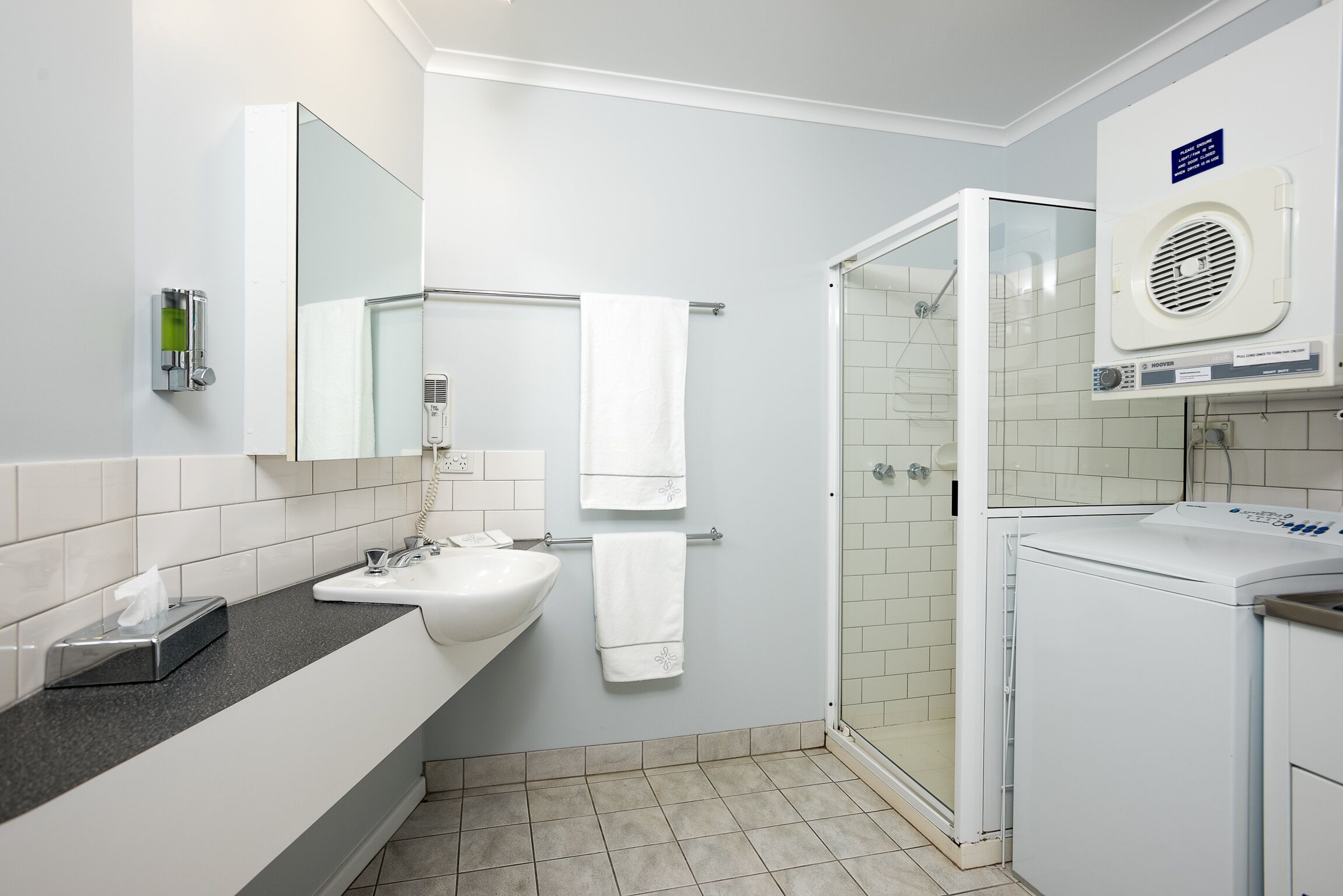 Ein modernes Badezimmer mit Waschbecken, Spiegel, Handtuchhalter, Dusche und integriertem Trockner.