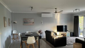 Un salon moderne comprenant un coin repas, un canapé en cuir noir, un téléviseur à écran plat et un ventilateur de plafond.
