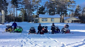 Un grupo de motos de nieve estacionadas en un campo nevado con casas al fondo.
