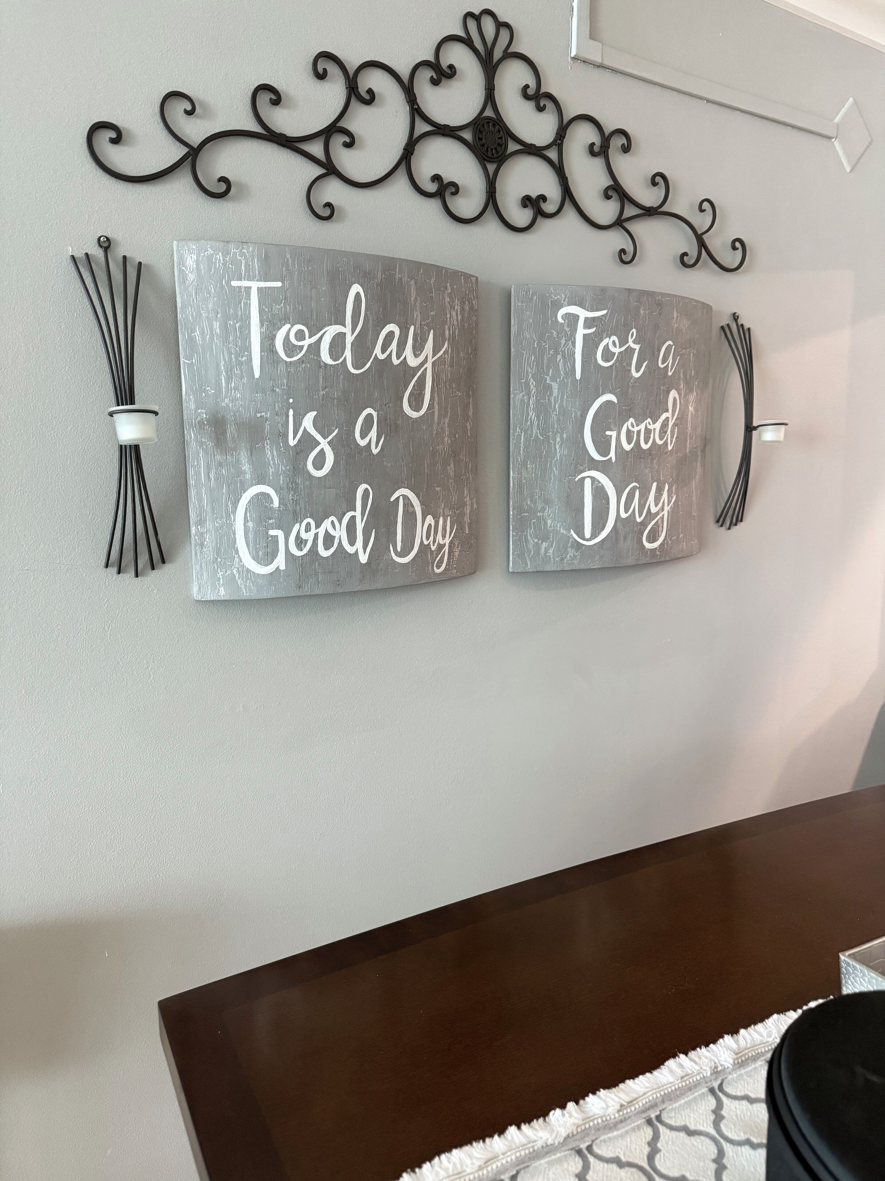 Two metallic wall decorations with the phrases "Today is a Good Day" and "For a Good Day" mounted on a wall above a dark wooden table.