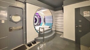 A futuristic room with a circular window, a bed, a handrail, and a sign indicating a hotel. - Astrotel Cubao (Quezon City)