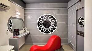A modern bathroom with a red bench, a circular wall decoration, and a shower area. - Astrotel Cubao (Quezon City)