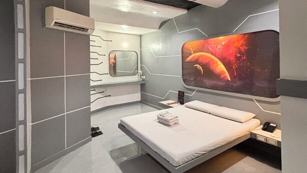 A modern hotel room with a bed, a large wall-mounted TV, a bathroom with a mirror, and a ceiling with a unique design. - Astrotel Cubao (Quezon City)