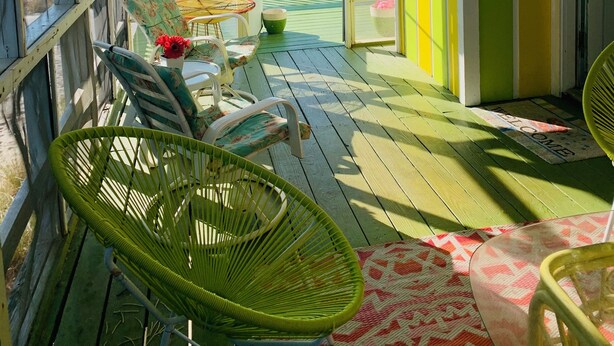 Un espacio al aire libre cubierto con vista a la playa, que incluye una mesa con sillas, un muro decorativo y una puerta.