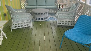 Un área de estar al aire libre techada con muebles de mimbre y piso verde.