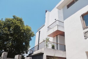 A modern building with a balcony, a clear sky, and a tree in the foreground.