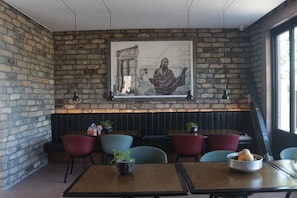 A restaurant with brick walls, a large mural, and booths with red and blue chairs.