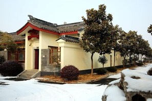 A traditional building with a tiled roof and a red door, surrounded by snow-covered ground and trees. - Lianyungang Donghai Shisu Onsen Villa (Lianyungang)