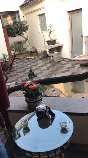 A small outdoor seating area with a table and chairs, a potted plant, and a view of a courtyard with a fountain and a building in the background. - Lianyungang Donghai Shisu Onsen Villa (Lianyungang)