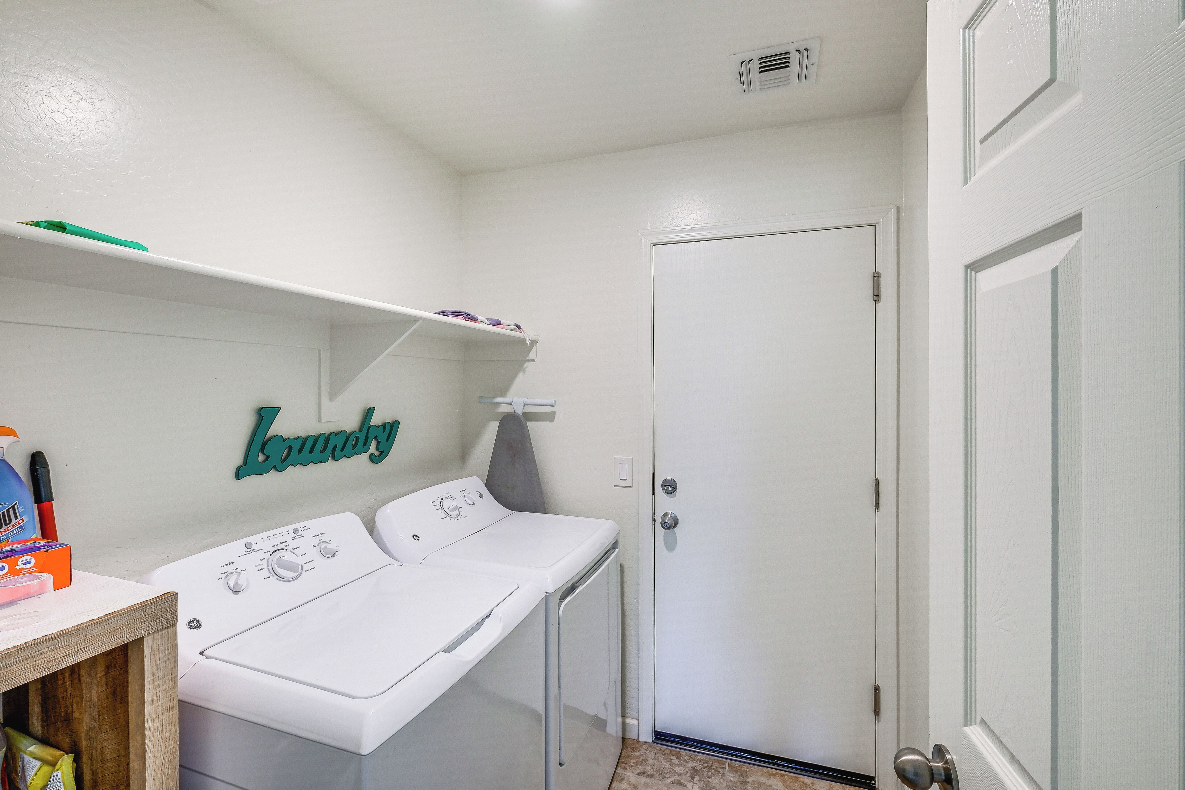 A laundry room with a washing machine and dryer, a shelf with laundry supplies, and a door.
