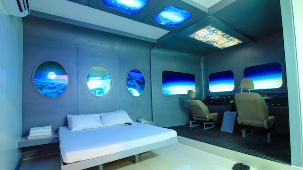 Una habitación moderna con una cama, dos sillas y un panel de control.