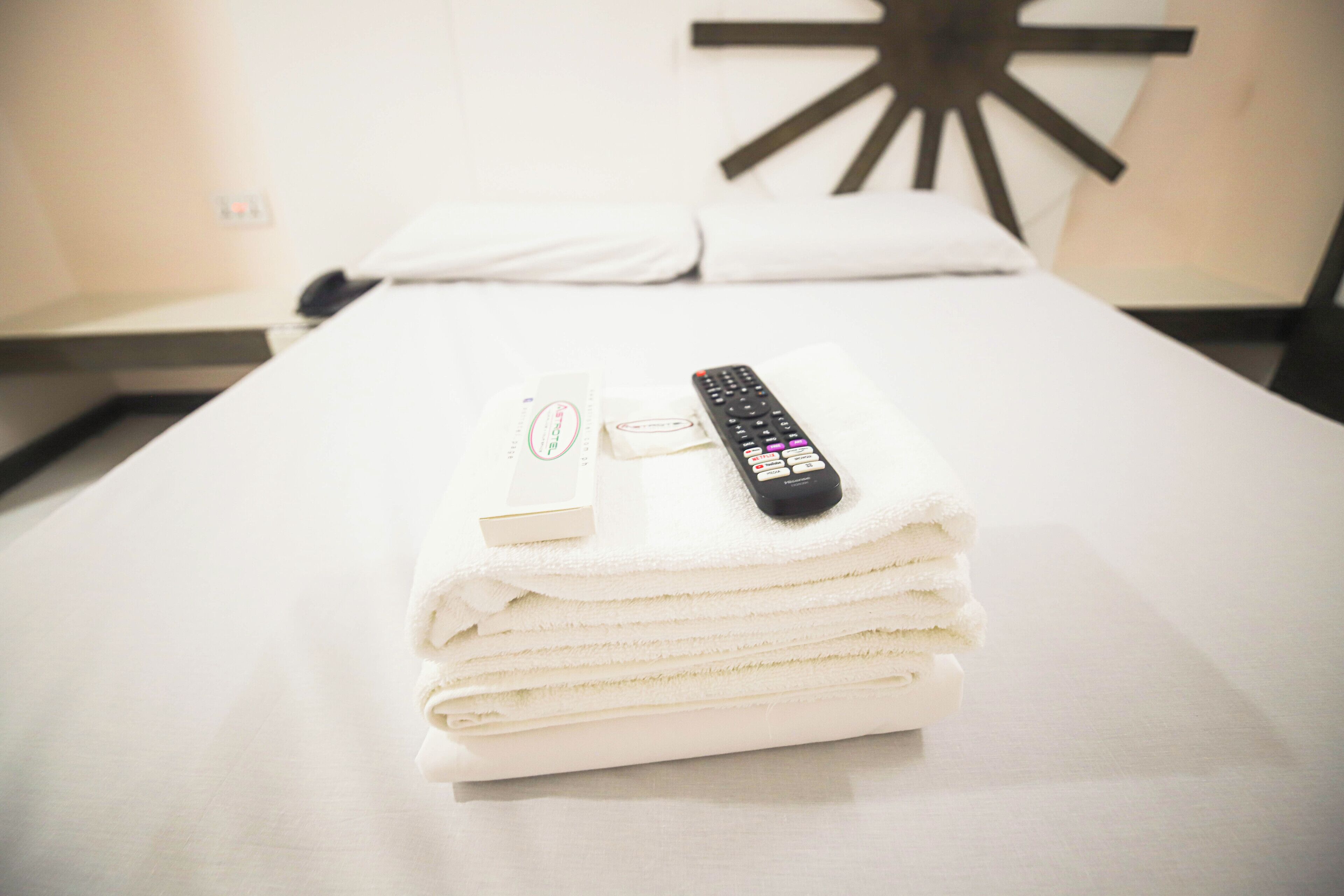 A neatly made bed with a remote control and a bottle of lotion on top.
