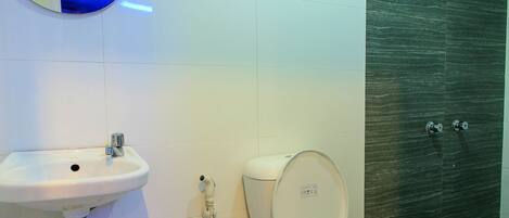 Un baño moderno con lavamanos, inodoro y zona de ducha blancos.