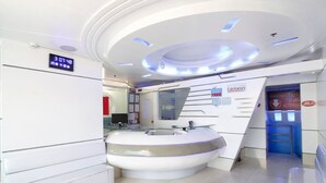 Un área de recepción moderna con un mostrador circular, un reloj digital y una escalera que conduce a un nivel superior.