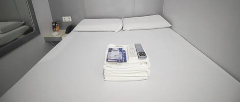 Una cama bien hecha con sábanas blancas, un control remoto y una toalla doblada en una habitación de hotel con pared gris y un mural con temática espacial.