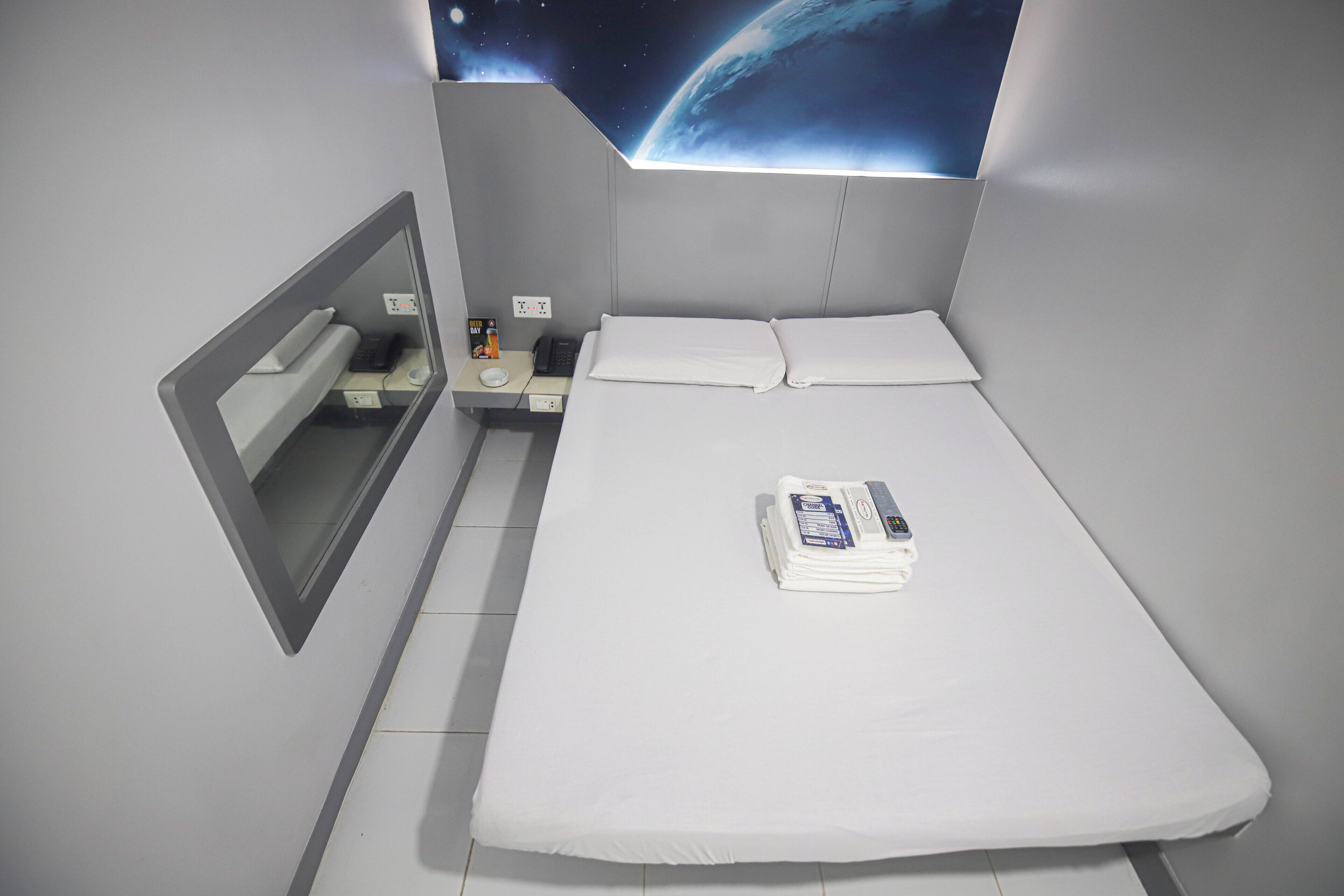 Una habitación de hotel moderna con una cama bien hecha, una mesita de noche con lámpara y un espejo en la pared.