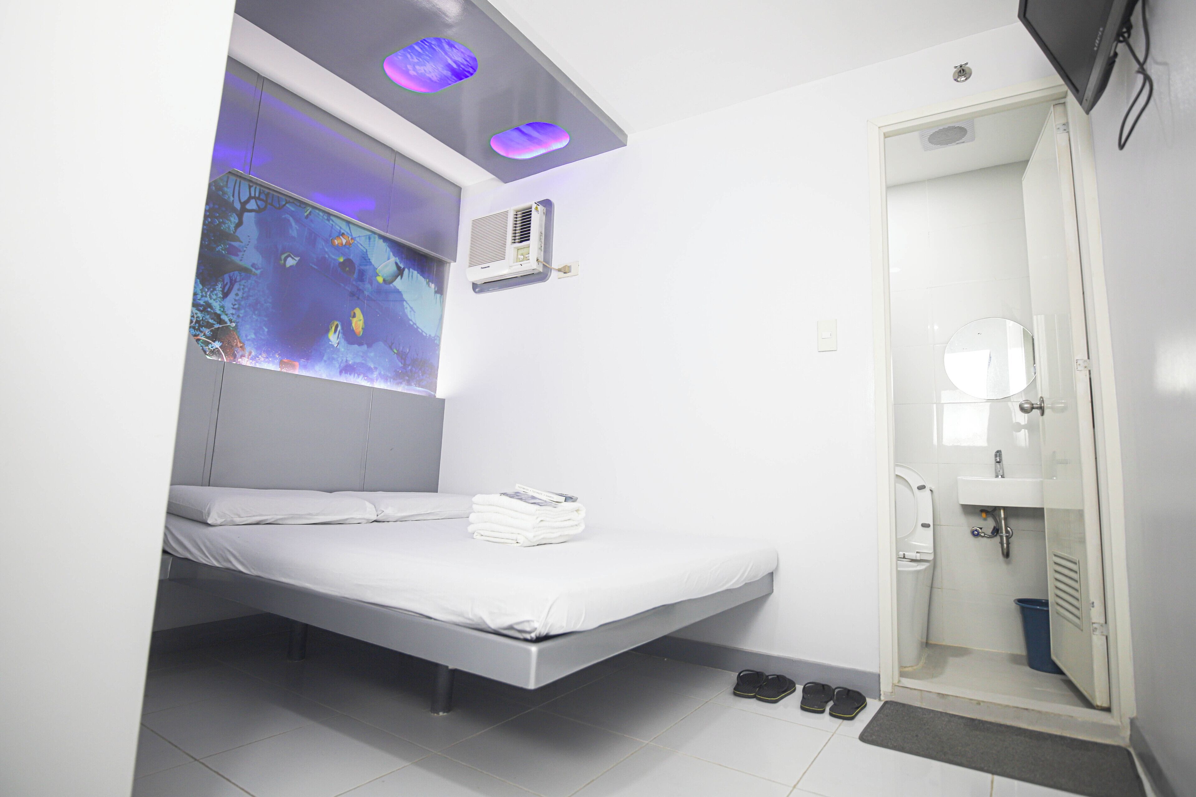 Una habitación pequeña y moderna con cama, ducha y aire acondicionado de pared.
