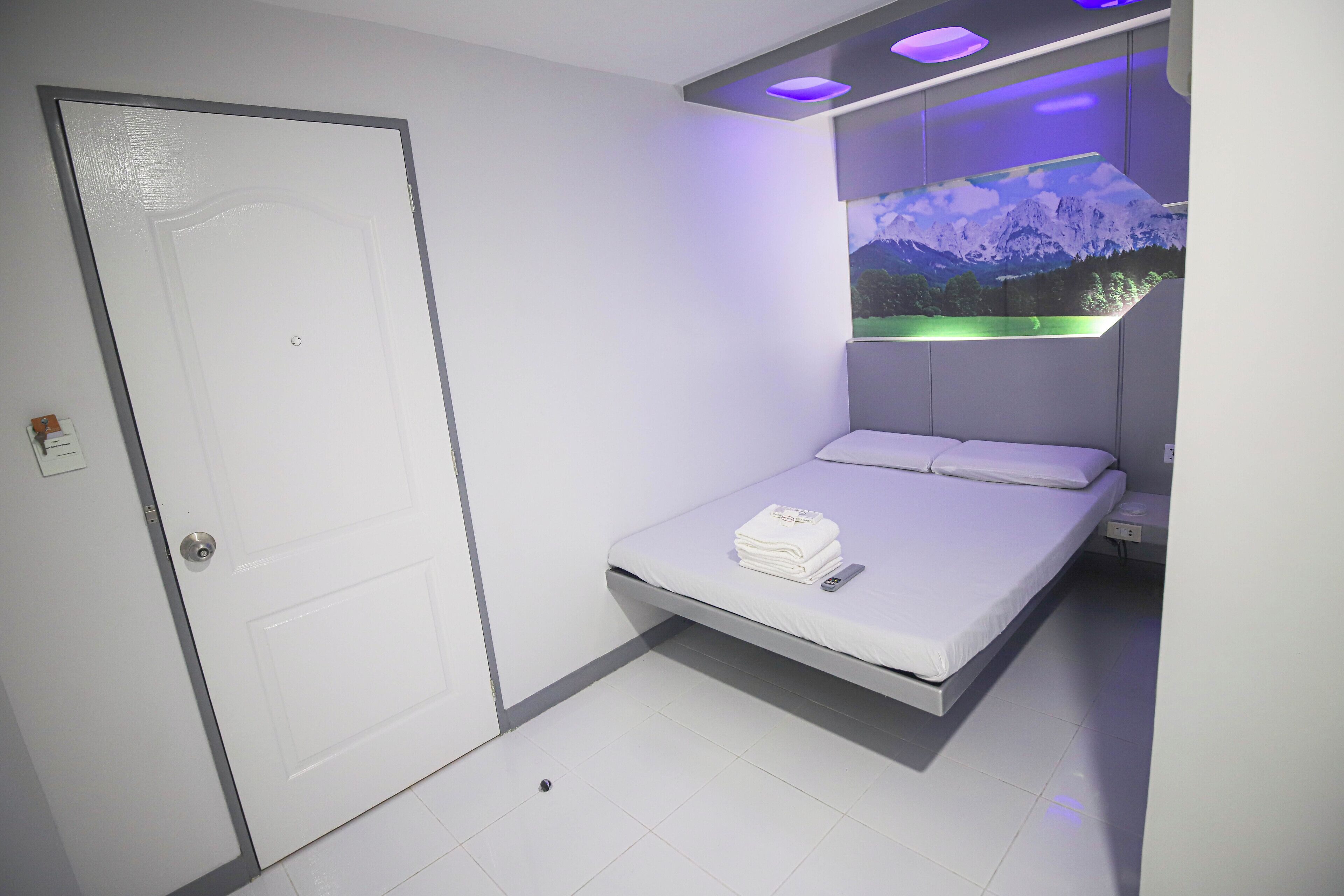 A modern hotel room with a single bed, a mounted TV, and a door with a lock.