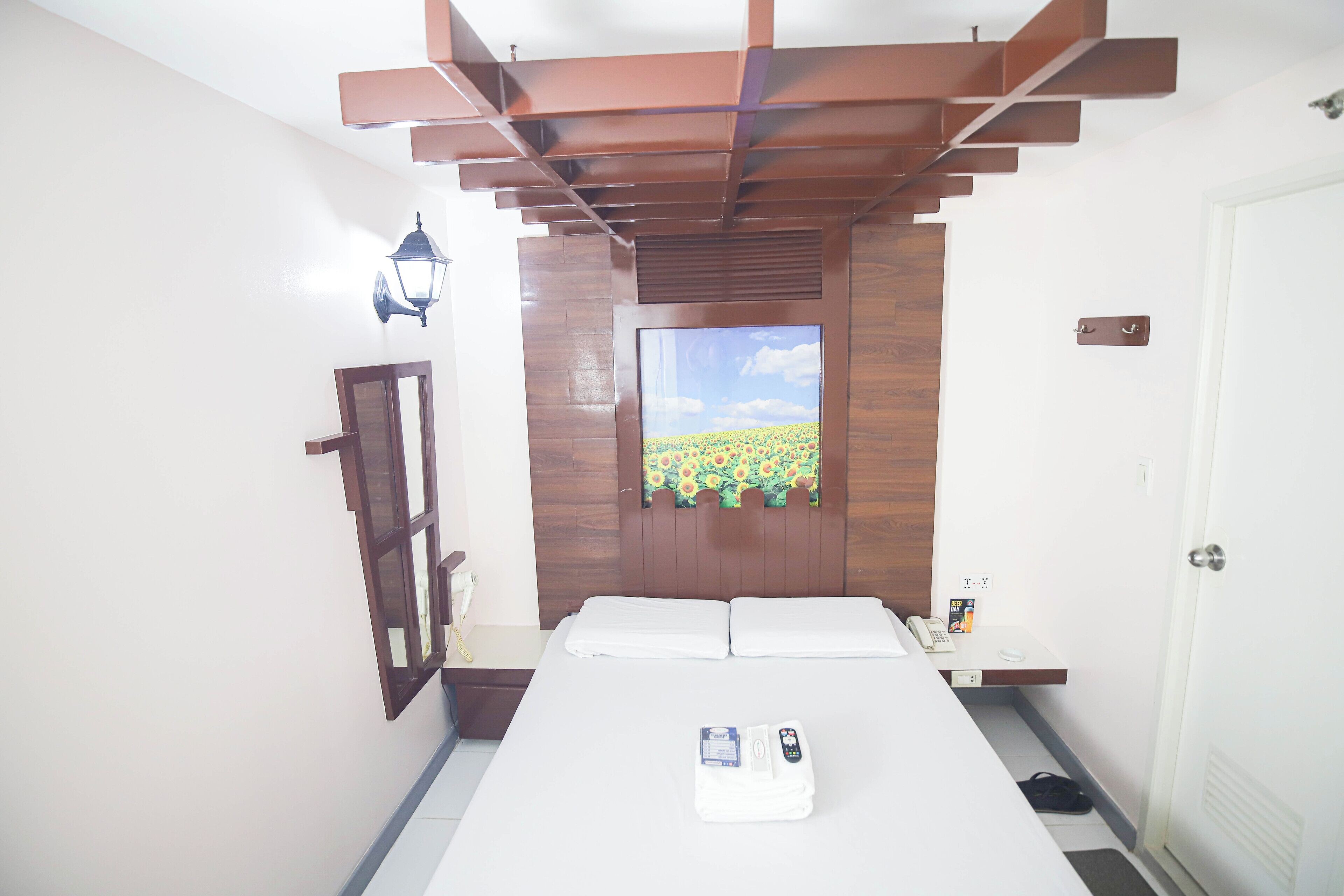 Habitación de hotel con cama, mesita de noche, televisor montado en la pared y puerta con manija.