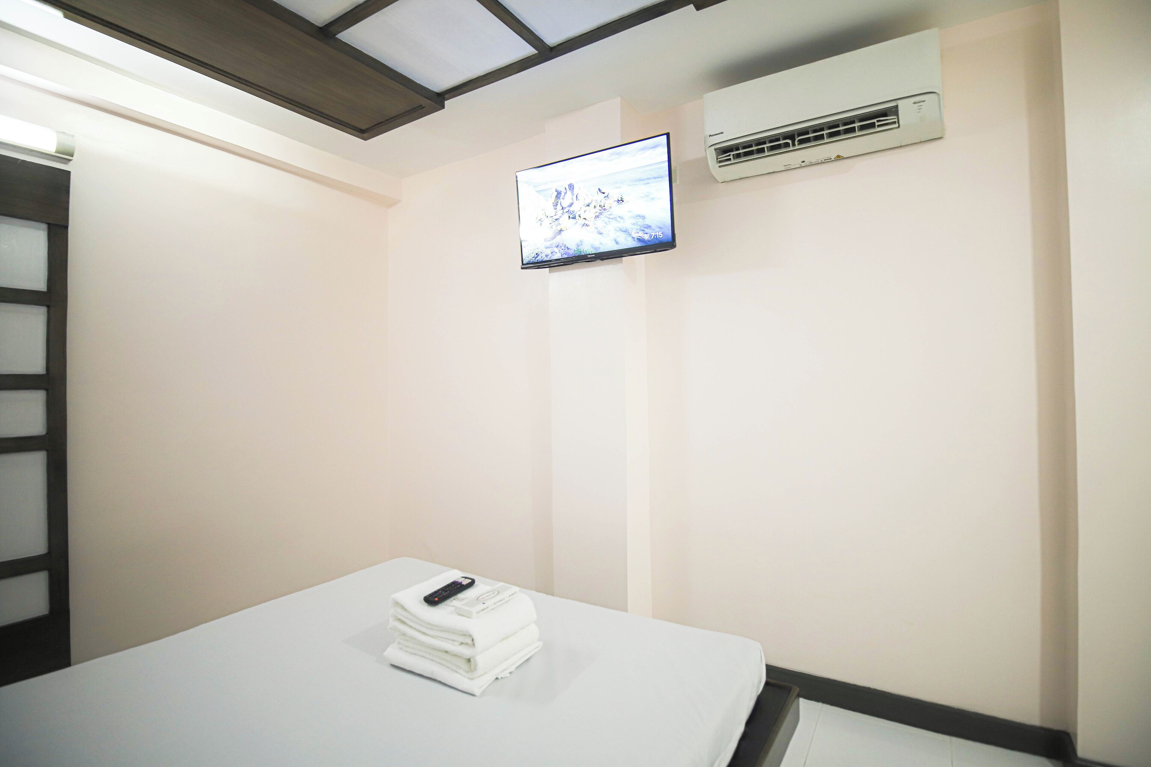 Una habitación de hotel con una cama, un televisor montado en la pared y un equipo de aire acondicionado.