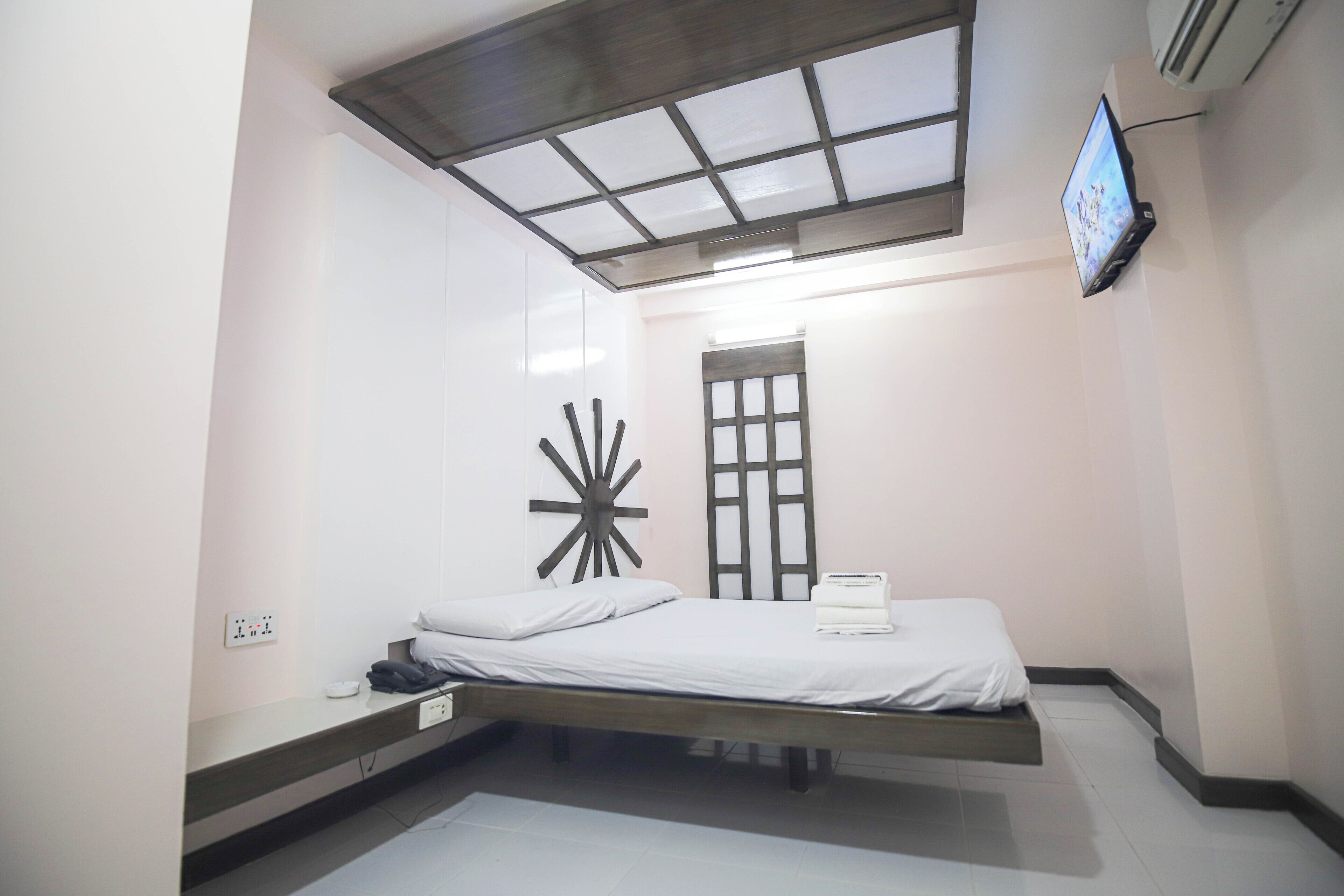 Un dormitorio compacto con cama, televisor montado en la pared y un diseño de techo original.