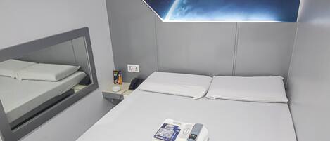 Habitación de hotel moderna con cama, mesita de noche, espejo, aire acondicionado de pared y decoración de pared con temática espacial.