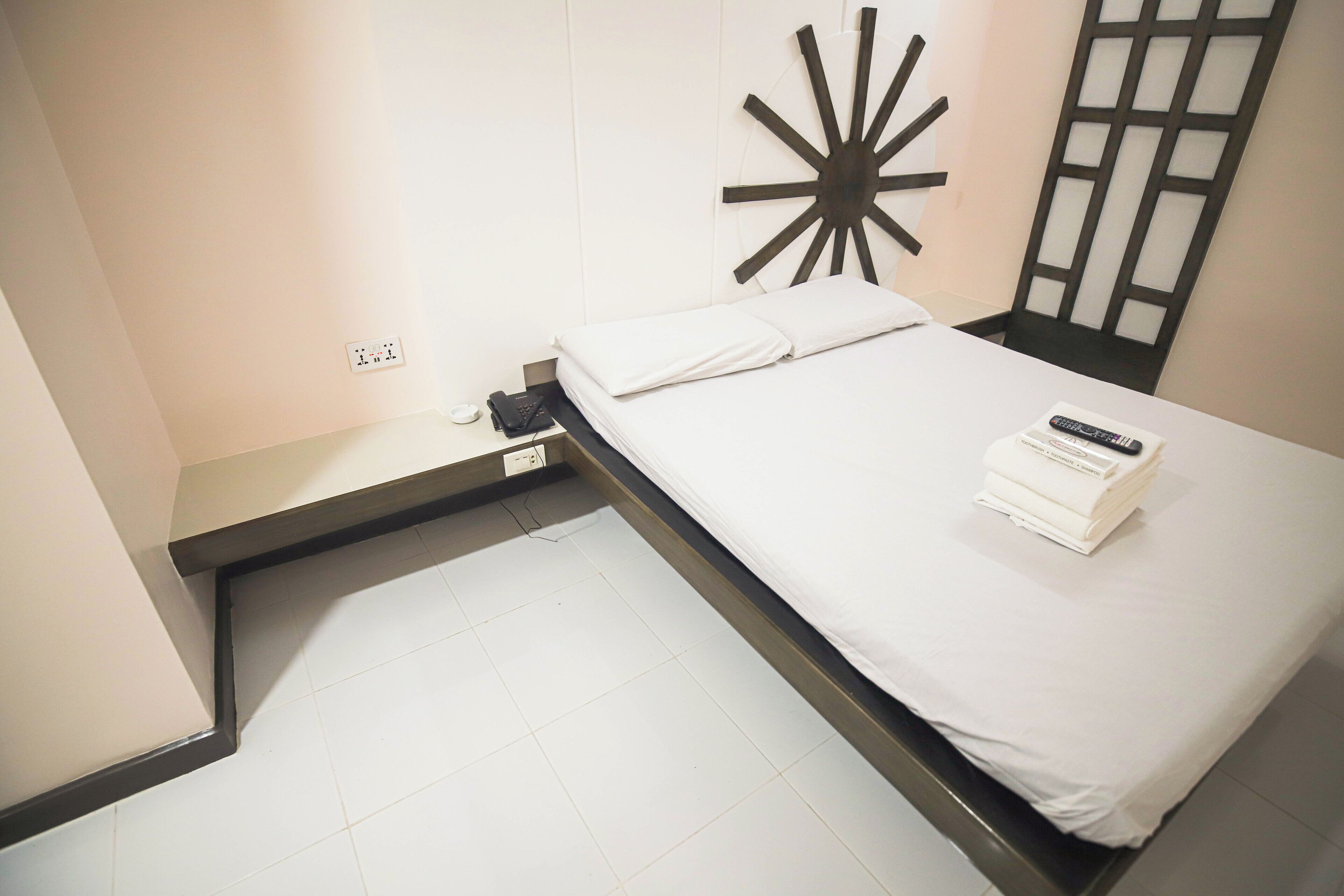 Een compacte, moderne hotelkamer met een bed, nachtkastje, een wandlamp en een stopcontact.