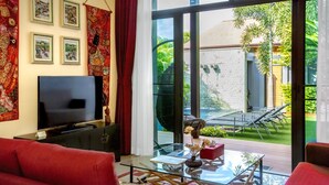 Ein modernes Wohnzimmer mit großem Fernseher, roten Sofas, einem Glastisch und Blick auf einen Garten mit Pool und Gartenmöbeln.