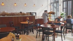 Ein Café mit Holztischen und -stühlen, einer weißen Ziegelwand und hängenden Pendelleuchten.