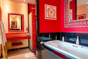 A modern bathroom with a red and black color scheme, a large mirror, a vanity with a red stool, and a bathtub with decorative items. - Almali Villa Mali (Rawai)