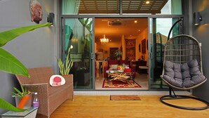 Ein modernes Interieur mit Glastür, einem Korbsessel, einem grauen Polsterstuhl und einem Essbereich mit einer roten Couch und einem Tisch.