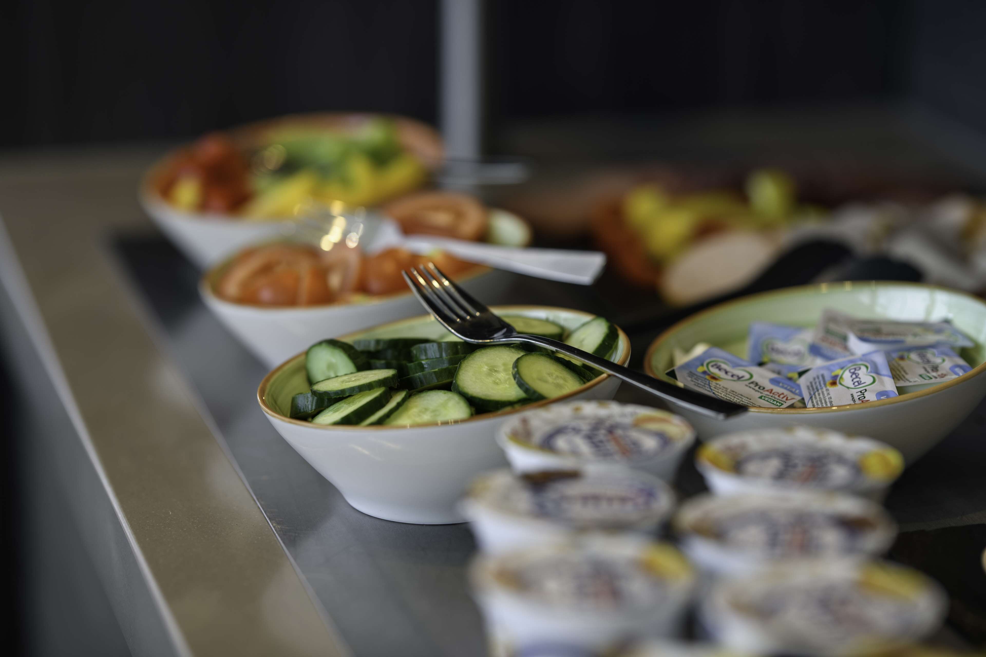 A buffet table with various dishes including a bowl of sliced cucumbers and a bowl of yogurt.