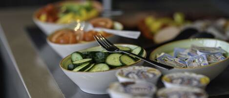 A buffet table with various dishes including a bowl of sliced cucumbers and a bowl of yogurt.
