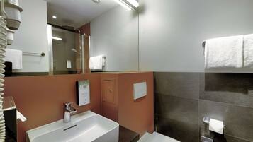 Une salle de bain moderne avec un lavabo blanc, un miroir, un porte-serviettes et un espace douche.