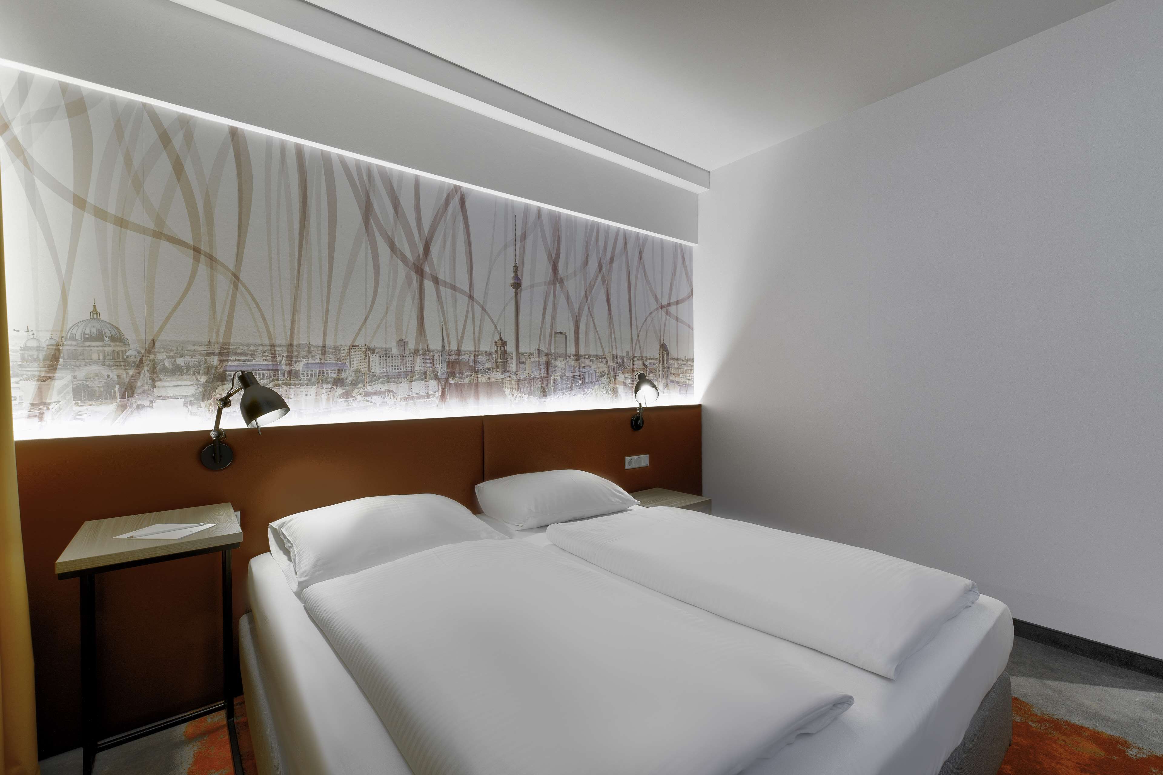 A hotel room with a large bed, a nightstand, a lamp, and a wall art depicting a cityscape.