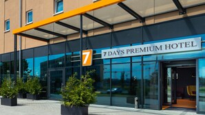 Exterior de un hotel moderno con fachada de vidrio, un llamativo letrero con el número 7 y un cartel que dice "7 DAYS PREMIUM HOTEL".