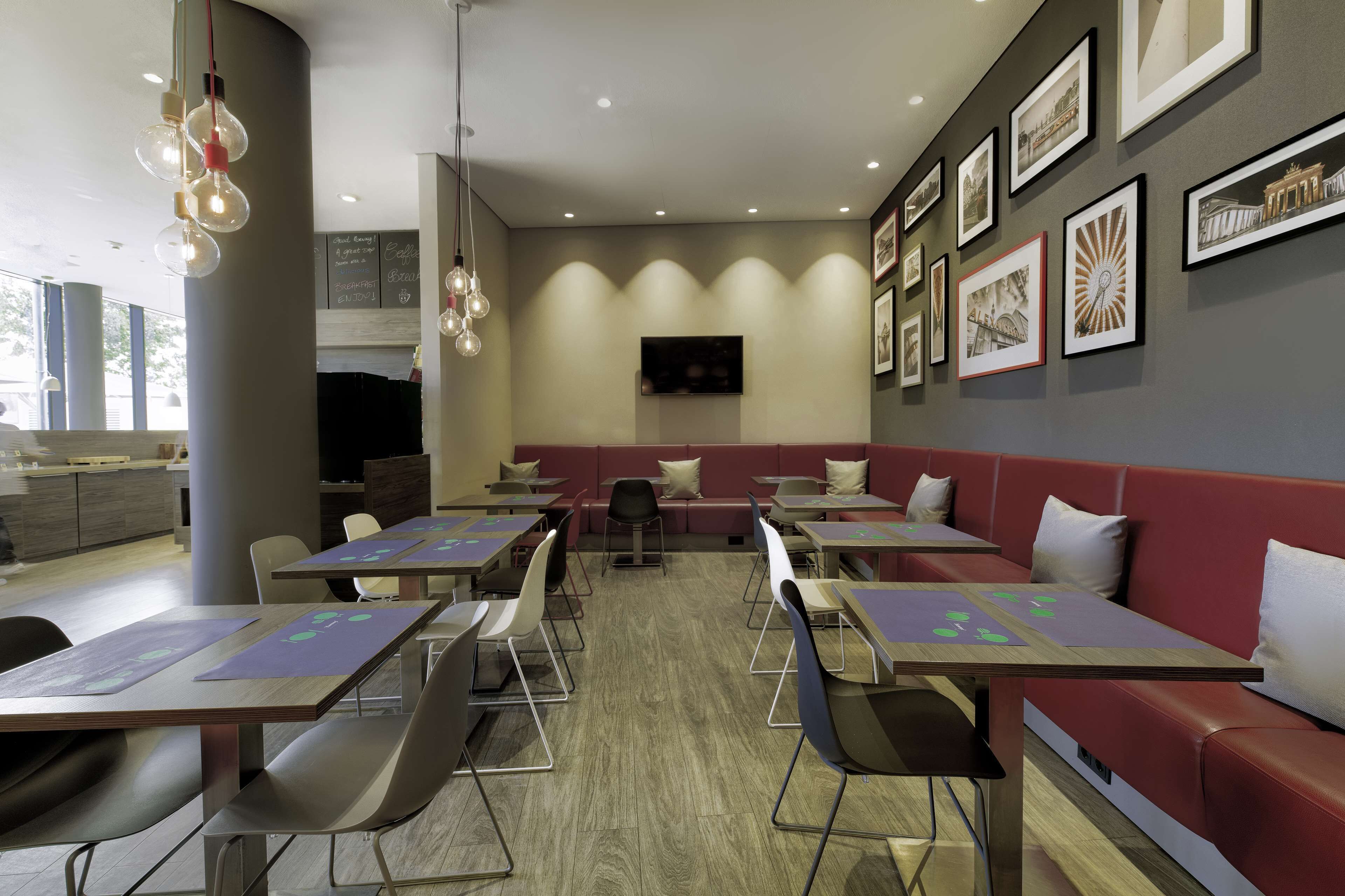 A modern restaurant with red booths and tables, framed pictures on the walls, and pendant lights.