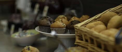 Variedad de productos horneados a la vista, como muffins y galletas, dispuestos sobre una mesa con una cesta y un bol.