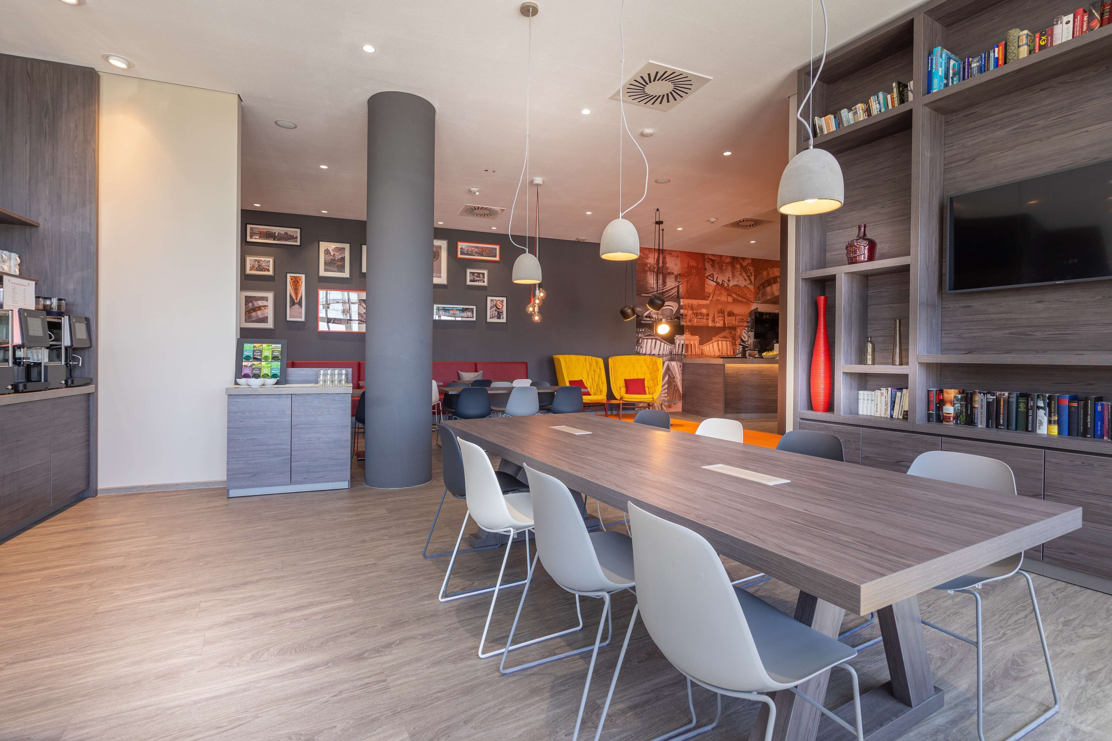 Une cuisine moderne dotée d’un îlot central, d’un coin repas avec une longue table et des chaises, et d’une bibliothèque contenant divers objets.