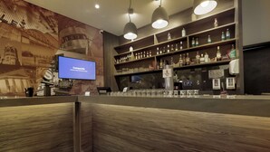 Zona de bar con estantes de madera llenos de botellas, vasos y una pantalla de televisión mostrando 'Compagnie'.